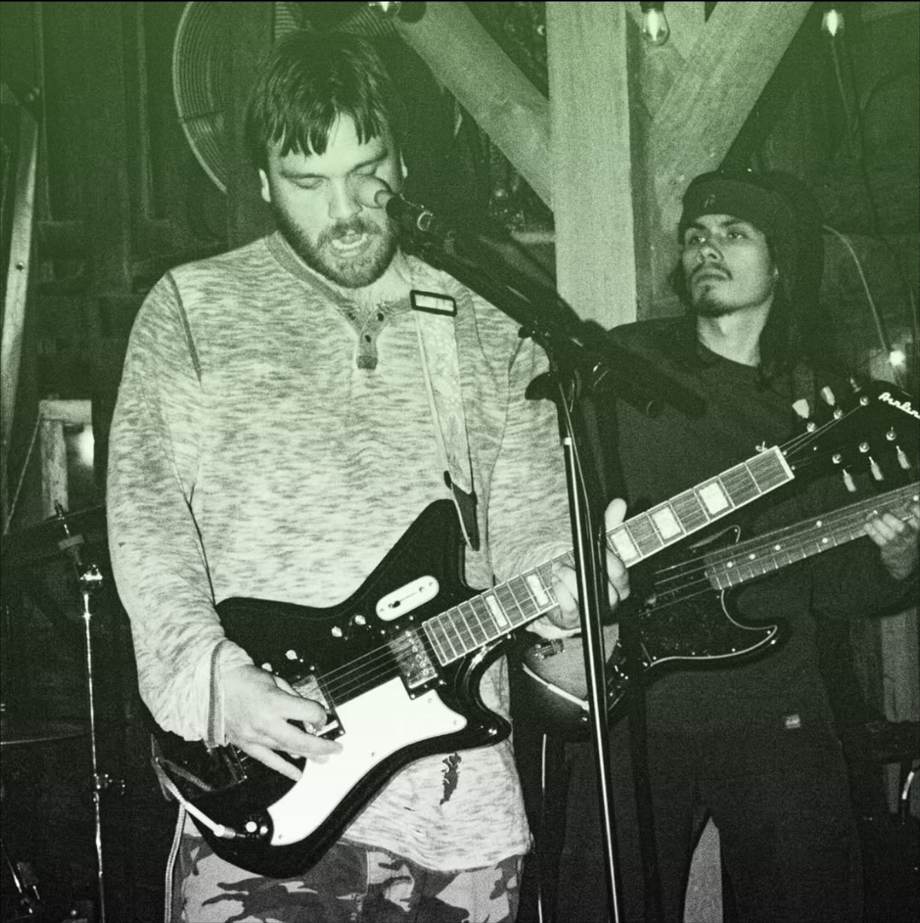 Two guitarists mid-set at the barn, in green-tinted black and white.